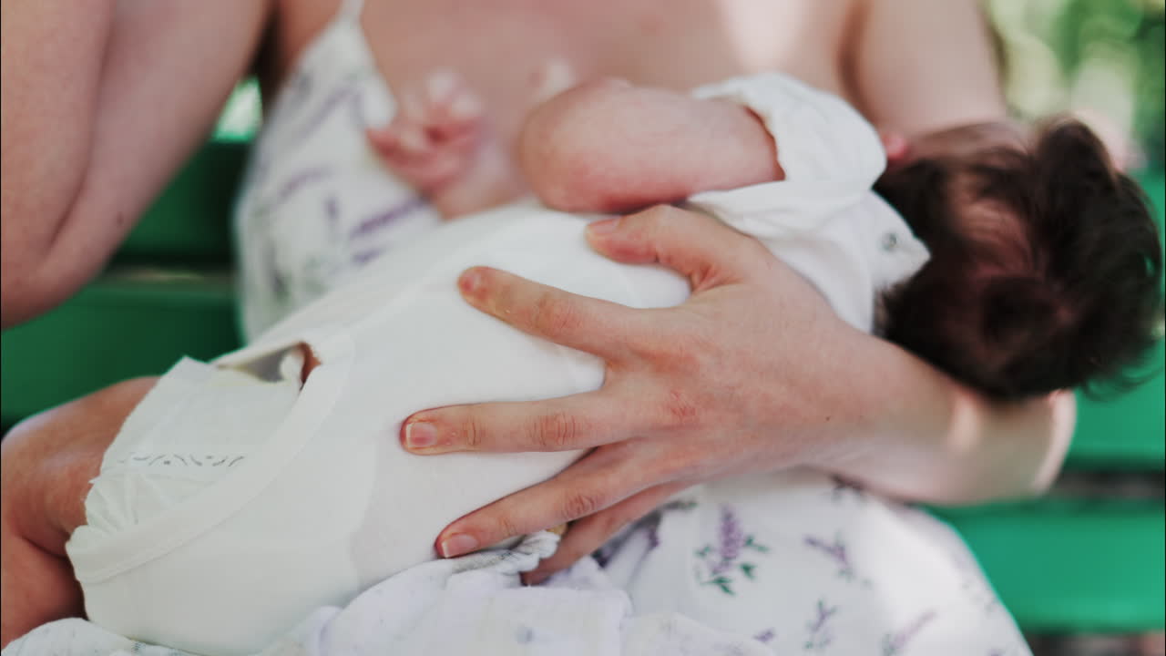 A mother siting on a bench in the park, breastfeeding her baby while enjoying a quiet, peaceful moment in nature