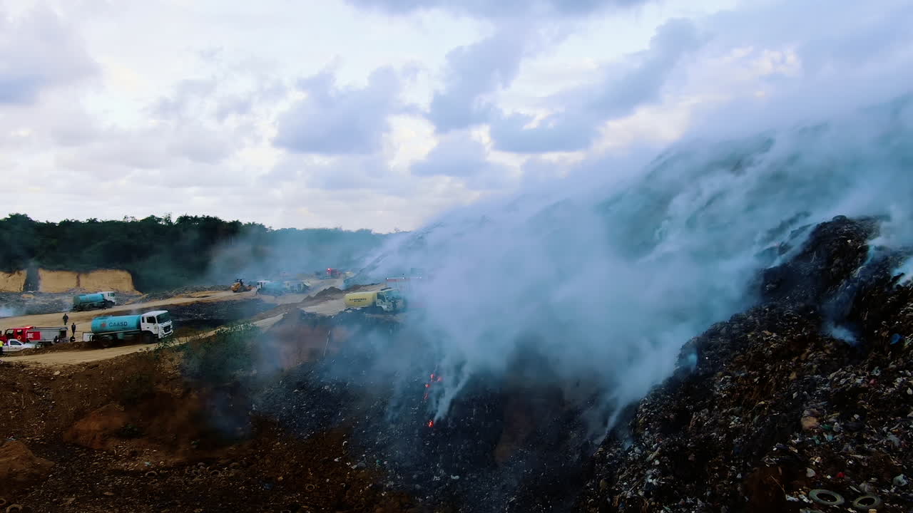 Ripresa aerea con drone attraverso fumo blu, camion dei pompieri e vigili del fuoco che cercano di domare l'incendio boschivo, sera nuvolosa, nella giungla amazzonica, Brasile, Sud America.