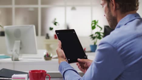 hombre de negocios caucásico teniendo una reunión de videollamadas usando una tableta en la oficina