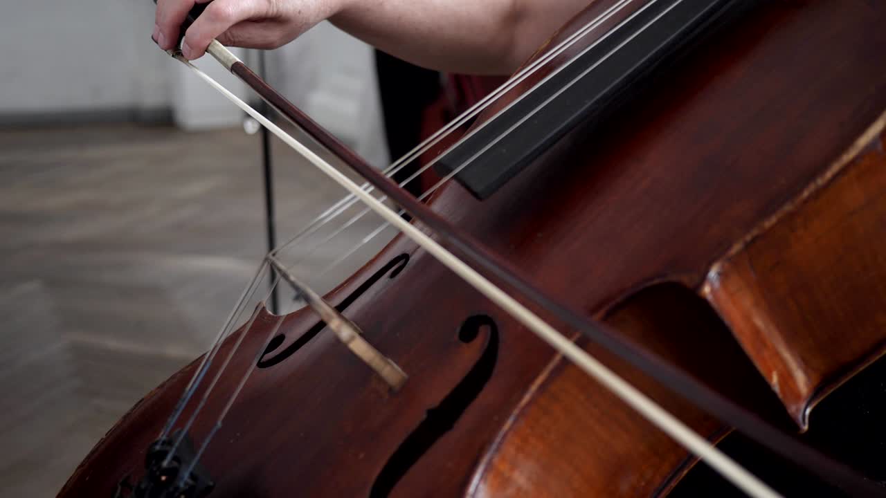 primer plano de un contrabajo con un violín-arco, mano femenina tocando el instrumento