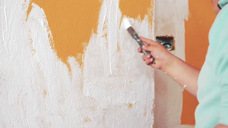 cute boy wearing cap using painting brush to paint orange wall into white color