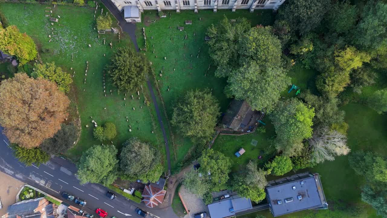 Aerial drone shot of Dorchester Abbey, Oxfordshire. Camera glides over trees and graveyard, then across the abbey roof, showing medieval stone architecture and modern solar panel features
