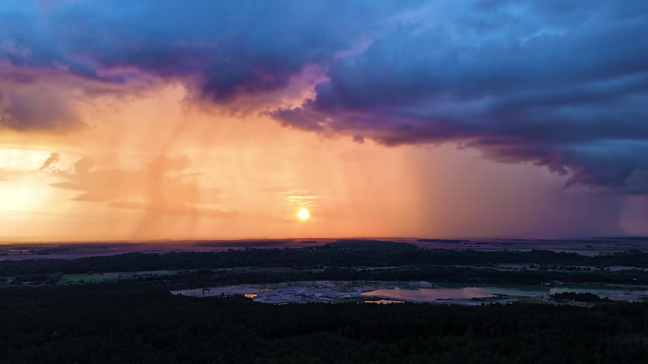 Vibrant orange sunset glowing through massive rainfall and dark clouds, aerial time lapse view
