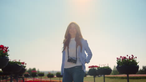 smiling girl in jeans standing with camera in blossomed spring park in sunshine.