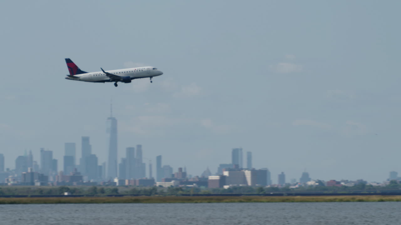 Delta Plane Passes in Front of New York City Skyline on Hazy Day with Camera Panning to Follow
