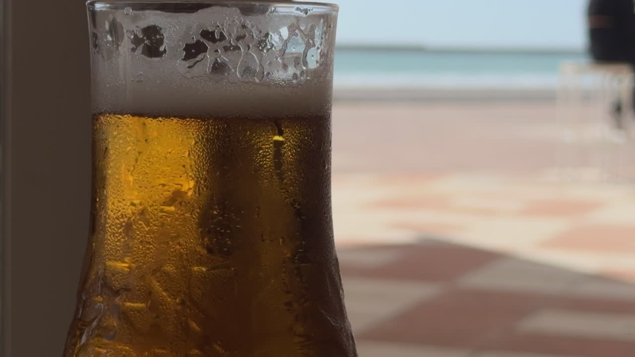 vista cercana de una cerveza con la playa detrás