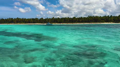 Das-Wunderschöne-Türkisfarbene-Wasser-Der-Karibik-Mit-Einem-Kleinen-Wasserfahrzeug,-Das-Am-Ufer-Der-Insel-Entlangfährt