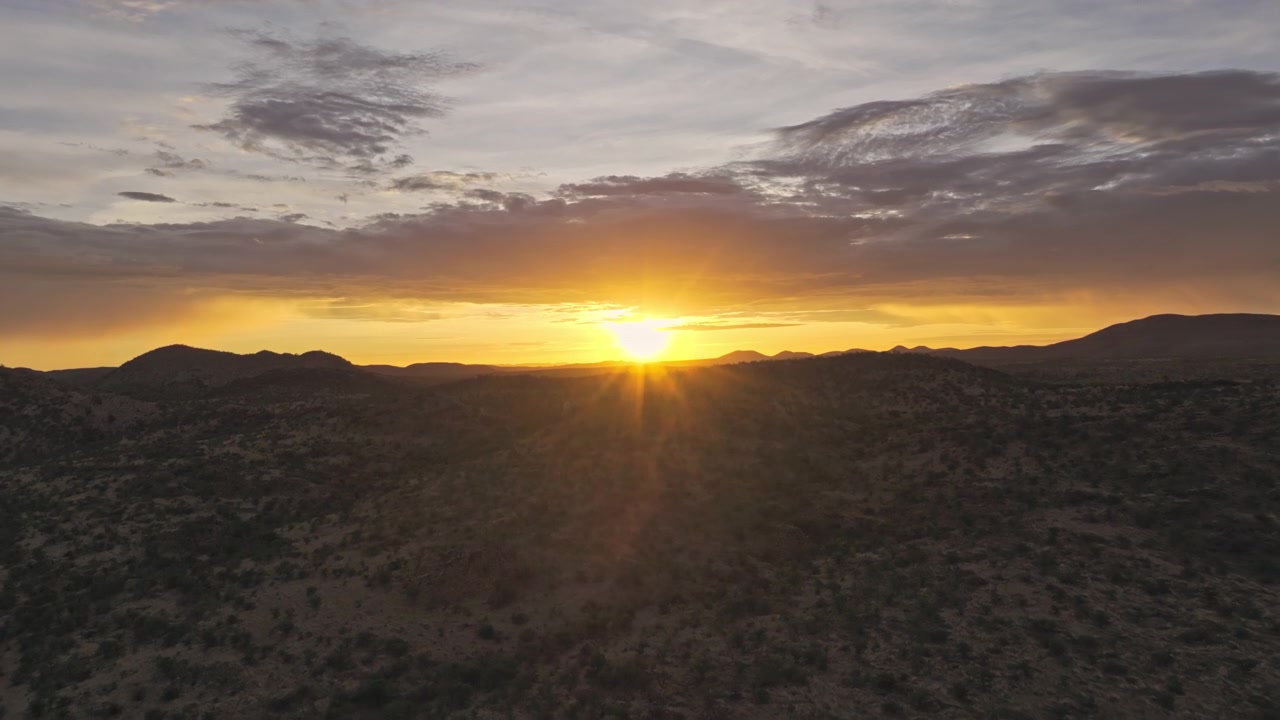 Drone footage of a warm golden sunset over layered desert ridges in central Namibia, soft evening light fading along the distant horizon.