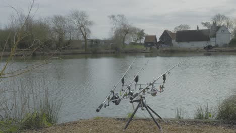 Close-up-shot-of-black-fishing-rods,-spinning-reel-for-carp-fishing-in-a-pond-in-Norfolk,-England-on-a-sunny-day