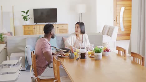 pareja feliz y diversa sentada a la mesa y desayunando