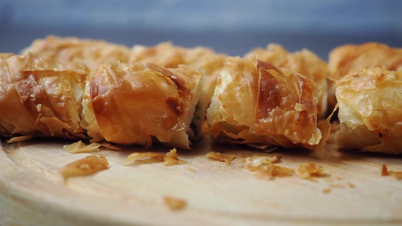 Primo piano di mani che affettano pasta fillo croccante su un tagliere di legno