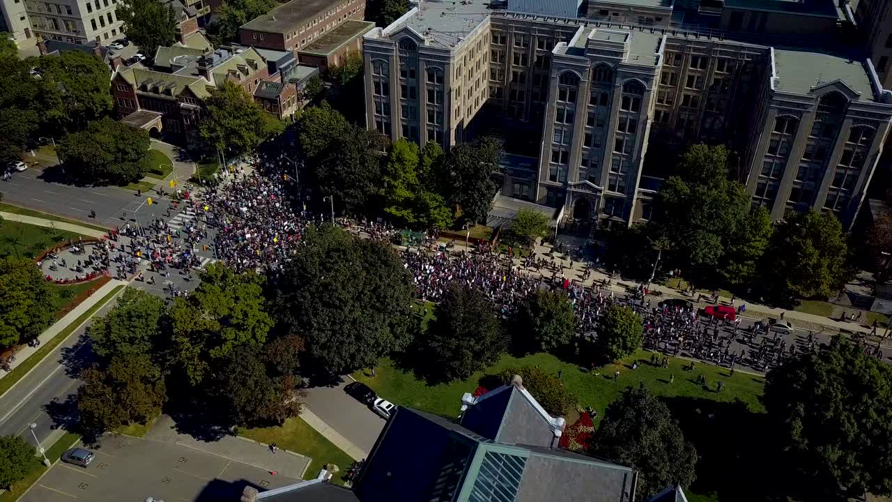 gran multitud marcha por edificios de piedra en toronto, antena drone pan