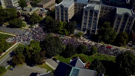 large crowd marches by stone buildings in toronto, aerial drone pan