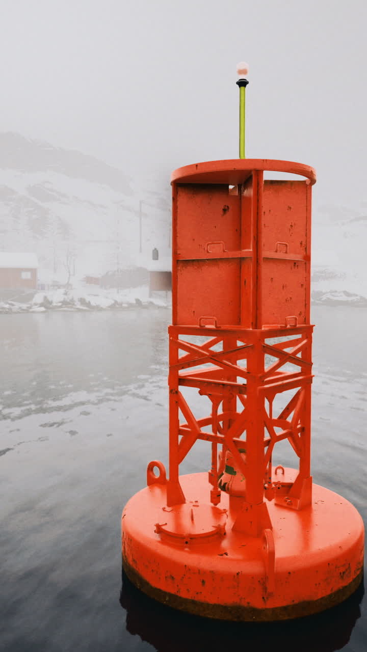 Bright orange buoy marking safe passage in foggy waters near coastal cabins