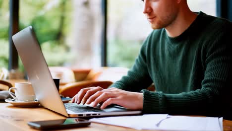 a man is typing on a laptop in a cafe