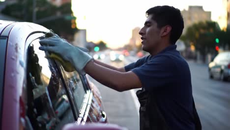 a dedicated worker polishing a car window as the sun sets, demonstrating the art of car care in a bustling urban environment