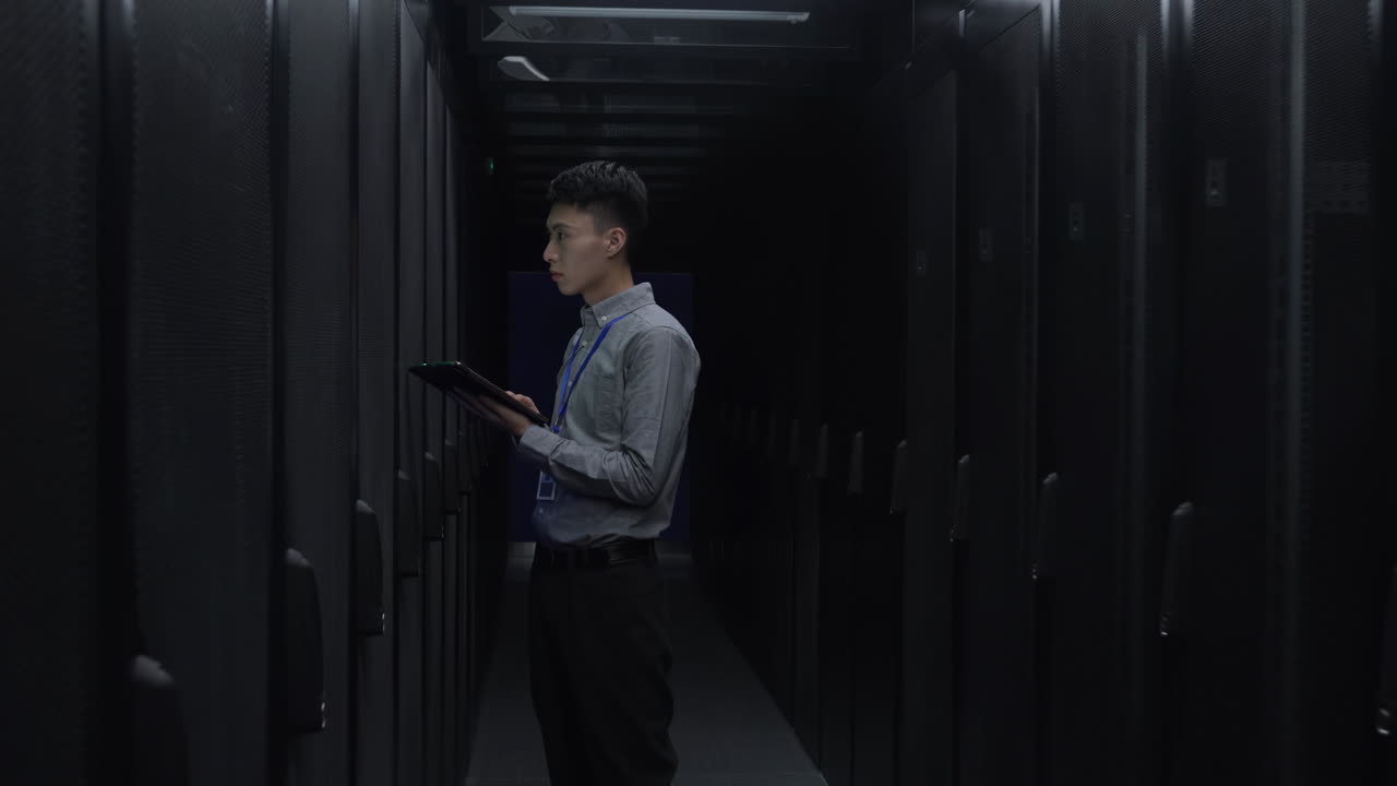 Male Professional Worker IT administrator In Engine Control server Room among rows of rack server cabinets and using laptop to check its work