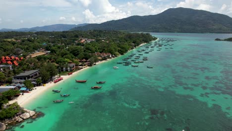 Koh-Lipe-Thailand-Coastline,-with-boats-and-hotels,-Ko-Adang-island-in-background--arial-fly-in