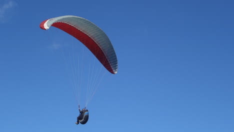 parapente debajo de un dosel rojo y blanco vuela cerca contra el cielo azul