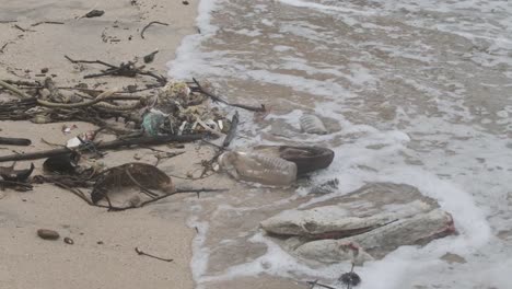 Waves-washing-up-on-a-sand-beach-covered-in-plastic-trash-garbage-rubbish-debris-slow-motion