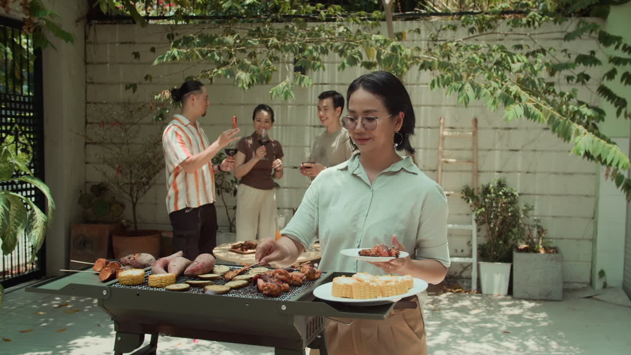 Portrait of Cheerful Asian Woman Preparing Corn on Grill during Party with Friends