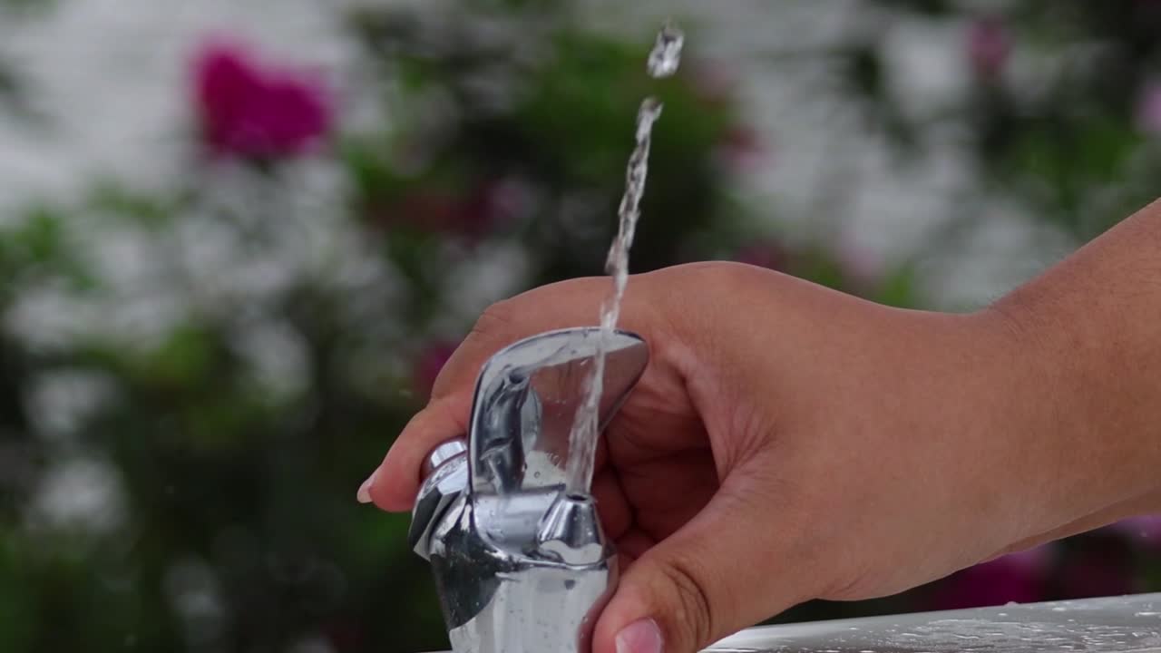 Een hand drukt op de hendel van een chromen drinkfontein om de waterstroom te stoppen