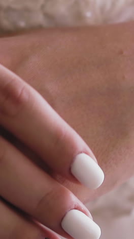cu, slow motion: elegant young lady in white dress holds gentle hands with beautiful pink and white manicure and word bride on nail extreme close view