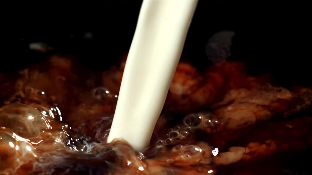 Latte cremoso che si versa nel caffè scuro al rallentatore