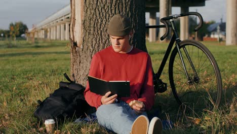 young man relaxing in park with bike and book