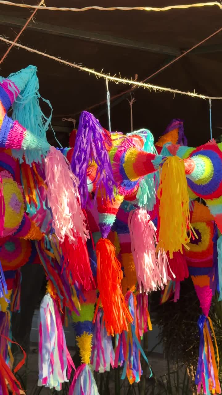 Colorful handmade piñatas hanging for sale at a market with bright tassels and festive designs