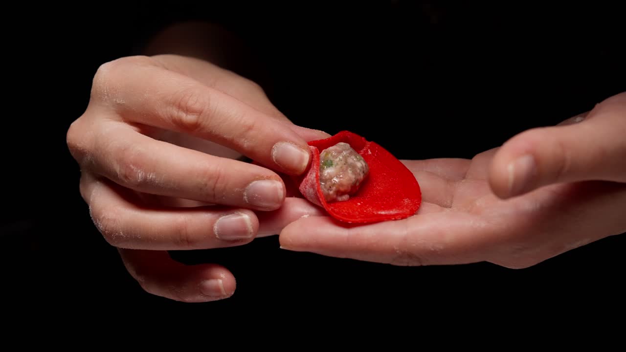 Primo piano di mani che piegano un raviolo rosso con ripieno