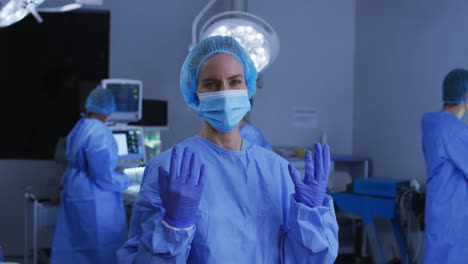 Portrait-of-caucasian-female-surgeon-wearing-face-mask-and-protective-clothing-in-operating-theatre