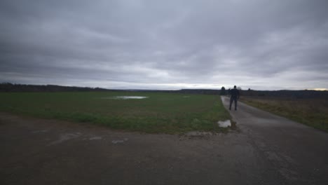 modern black swordsman warrior awaiting battle opponent in open field under grey sky, europe, 4k | muscular, intimidating, shadow, figure, blurry, dark clothes, powerful, distant patrol, turn around