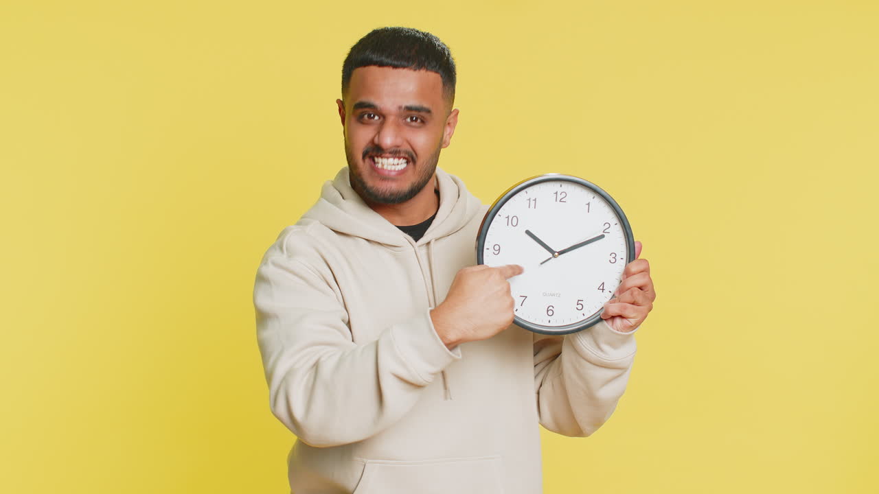 Indian young man showing time hour on wall office clock ok thumb up approve hurry up deadline