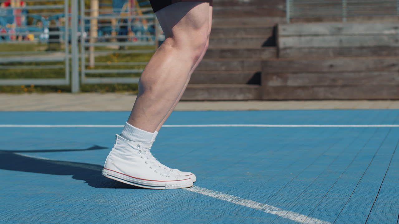 Closeup of athletic man legs skipping rope doing jumping exercises on basketball court outdoors