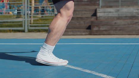 closeup of athletic man legs skipping rope doing jumping exercises on basketball court outdoors