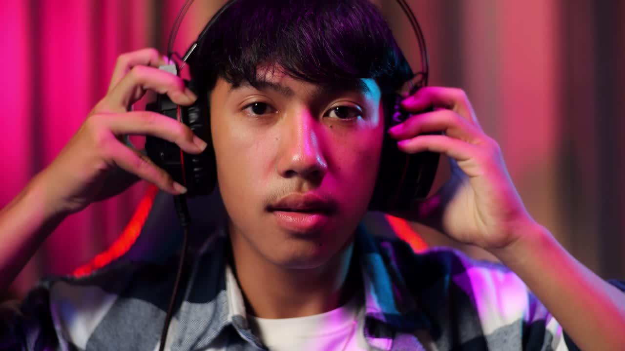 앞면의 가까운 시각에서 아시아 십대 소년 게이머가 헤드폰을 착용하고 컴퓨터에서 비디오 게임을 시작합니다.