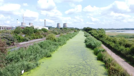 綠色藻類覆蓋的運河水道通往發電廠的工業空中無人機景觀