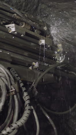 machinery equipment drills large hole in hard rock of ore mine to set explosives. robot drill with coolant operates spraying cold water closeup