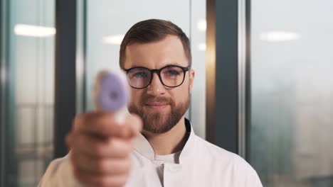 el retrato de primer plano de un médico varón que mide la temperatura con un termómetro sin contacto y sonríe