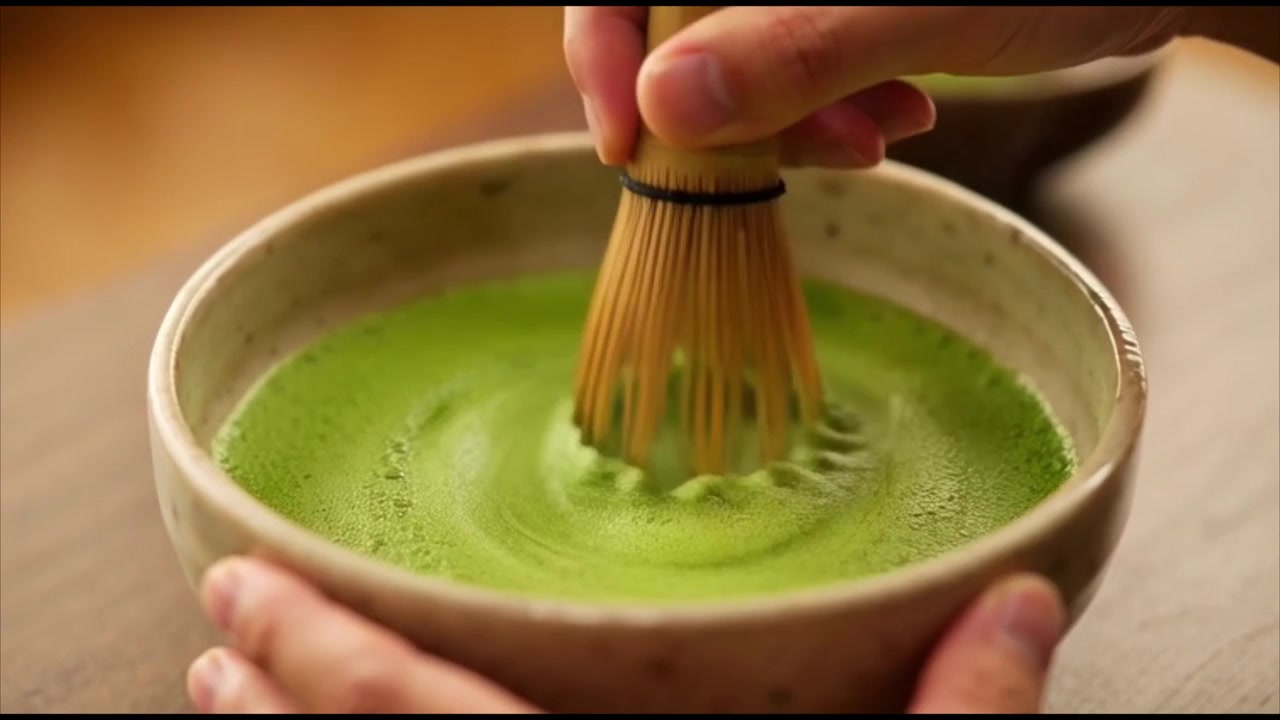 Pessoa batendo chá verde Matcha em uma tigela de cerâmica.