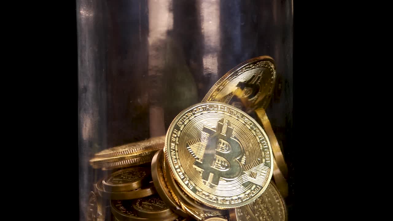 Monete di criptovaluta dorate e lucenti cadono in un barattolo di vetro trasparente, illuminate da una luce calda e riflettente