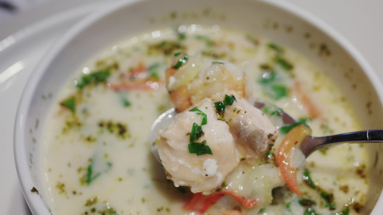 Primo piano di zuppa cremosa di salmone con erbe aromatiche e verdure, mescolata con un cucchiaio