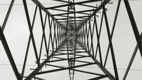 Look-up-inside-a-huge-steel-power-pole-on-a-cloudy-day,-electricity-distribution