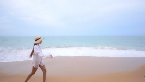 Cámara-Lenta-De-Una-Linda-Mujer-Joven-Con-Traje-De-Baño-Blanco-Caminando-Por-Una-Playa-De-Arena-Mientras-Las-Olas-Entran