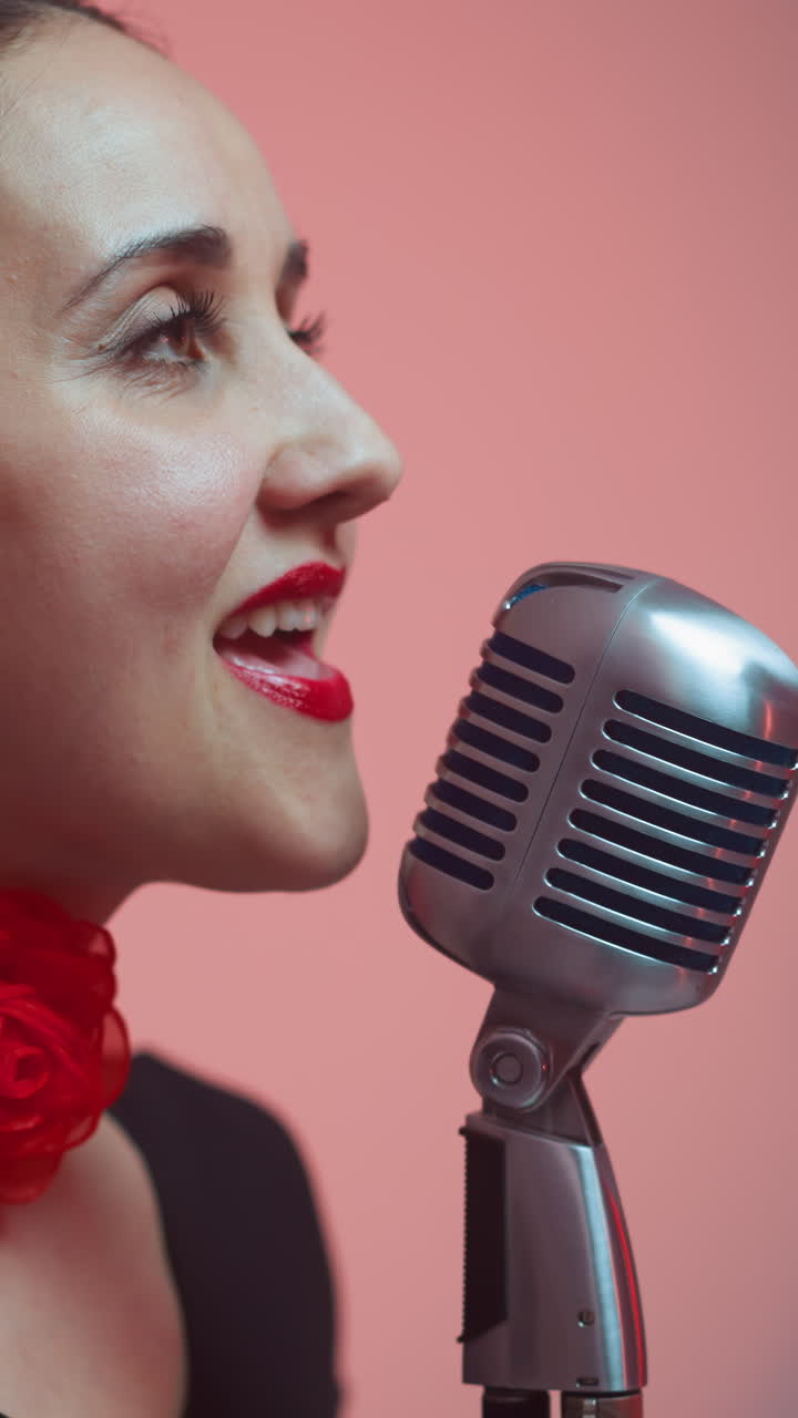 primer plano de una cantante apasionada con labios rojos, con una cinta roja en el cuello, cantando en un micrófono vintage, mientras la cámara se aleja lentamente