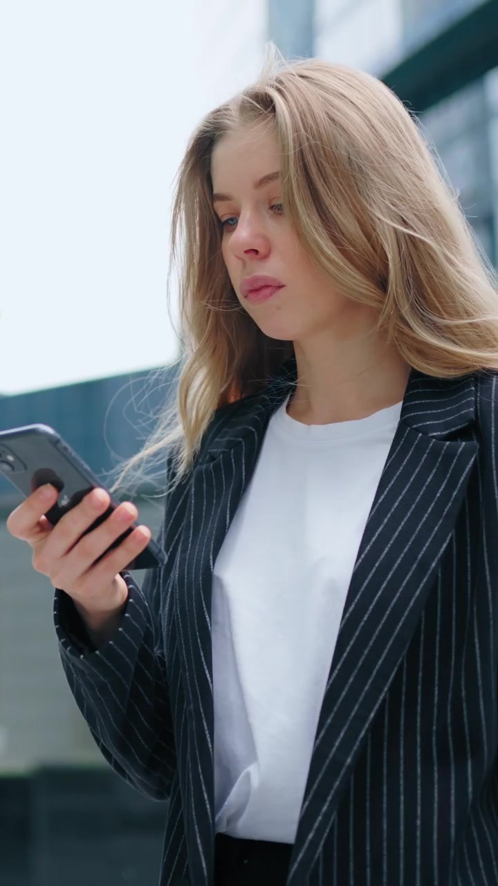 Giovane donna d'affari che usa lo smartphone all'esterno di un moderno palazzo per uffici