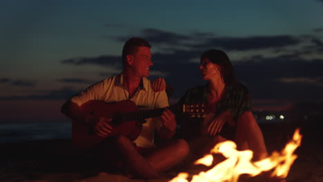 couple playing guitar by a campfire on the beach at sunset