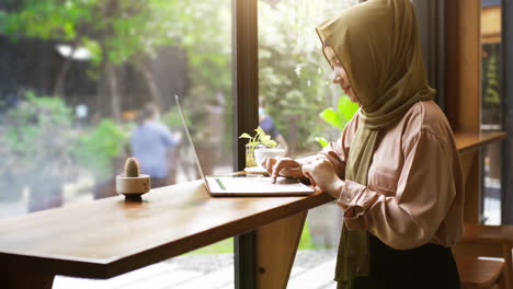 Una-Mujer-Musulmana-Asiática-Con-Movilidad-Ascendente-Que-Disfruta-De-Un-Momento-Relajante-En-La-Cafetería-En-Un-Día-Soleado