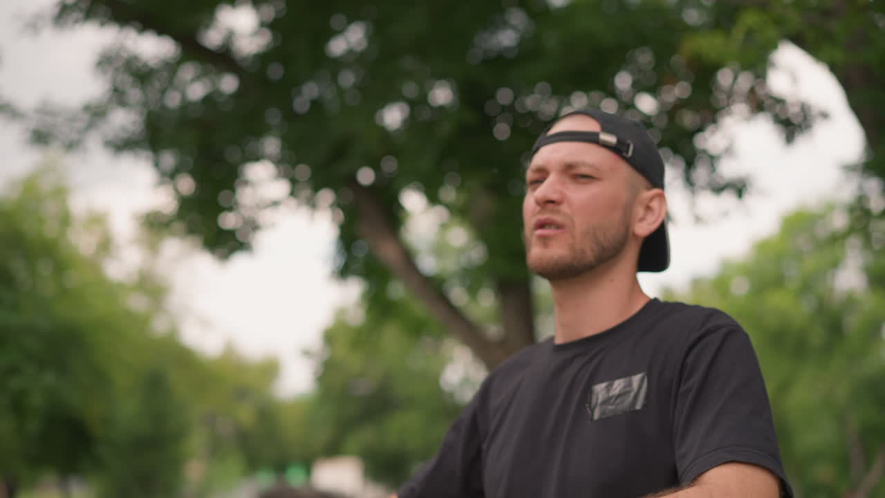 White Man Outdoors Rubbing Neck During Park Stretch, Cap Worn Backwards, Grimace Showing Discomfort And Momentary Relief, Summer Trees Background, Candid Closeup Of Facial Expression And Shoulder